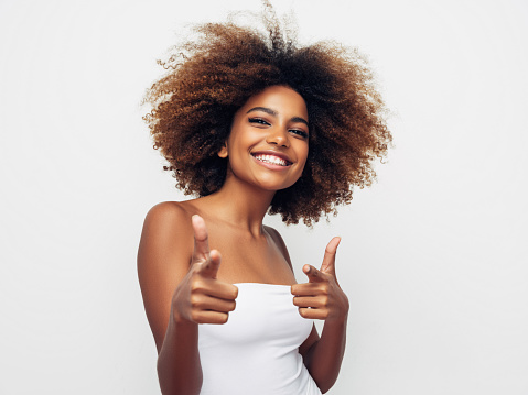 Young adult smiling woman against an orange yellow background is fixing her hair. Afro hair.