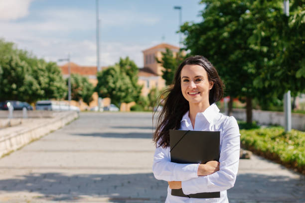 happy adult student poses looking at camera on college campus.senior and street student concept. - graduation student women beauty imagens e fotografias de stock