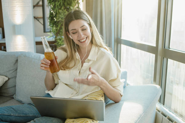 若い女性はオンラインパーティーに出席し、自宅でビールを飲んでいます - after work beautiful people beer beer bottle ストックフォトと画像