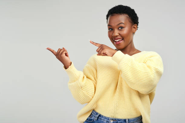 Shot of a young woman pointing at copy-space while posing against a grey background