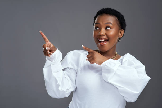istock Shot of a young woman pointing at copy-space while posing against a grey background 1325102579