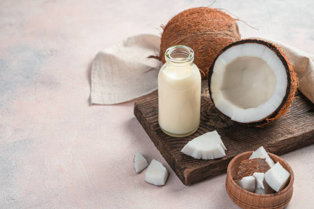 A bottle of coconut milk and a coconut on a light pink background Vegetable milk, a healthy drink made from coconut. A bottle of coconut milk and a coconut on a light pink background. coconut milk stock pictures, royalty-free photos & images