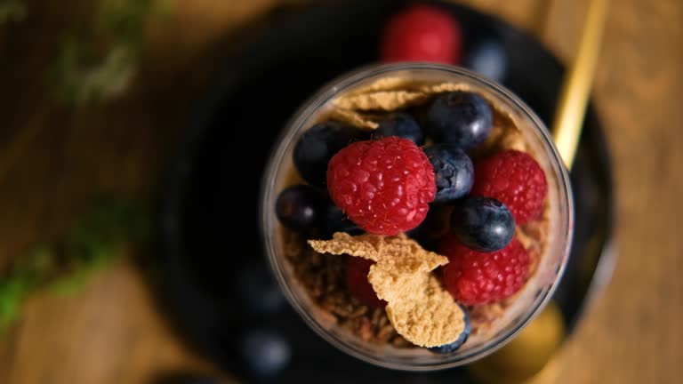 Top down view on granola with yogurt and berries for healthy breakfast on a wooden table. Dark style photography.