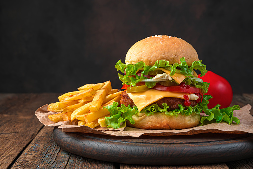 A large homemade burger and French fries on a brown background. Side view, copy space.