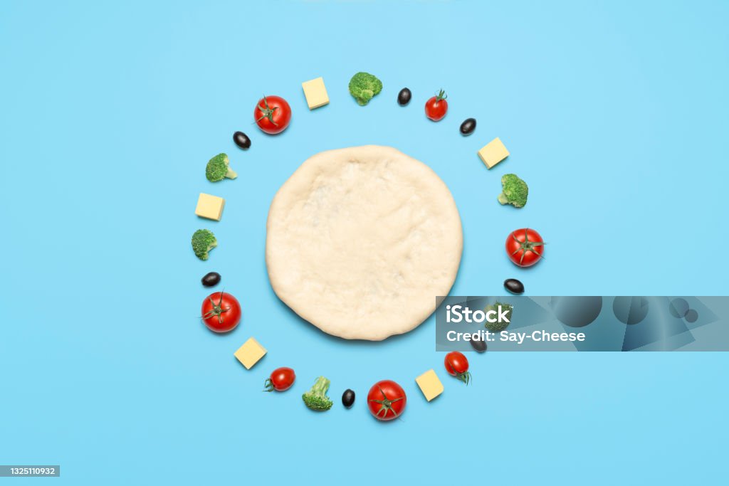 Vegan pizza ingredients, top view. Raw pizza dough and vegetables on blue table Making vegan pizza with vegetables and vegetarian cheese, isolated on blue-colored background. Flat lay, pizza dough and topping ingredients aligned Knolling - Concept Stock Photo