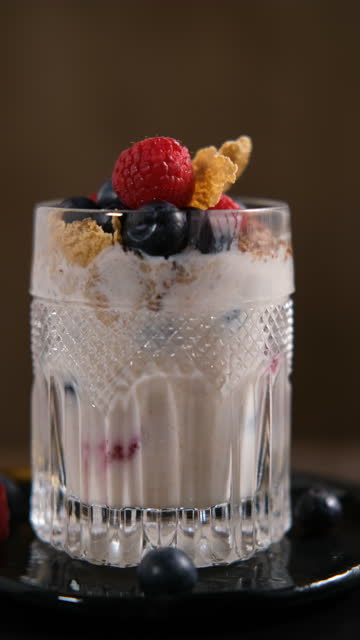 Healthy breakfast in rustic style - granola, corn flakes and fresh, ripe raspberries and blueberries in a fancy glass standing on a wooden table.