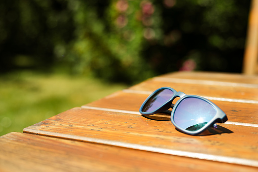 Holiday and vacation - blue sunglasses on the wooden table in garden