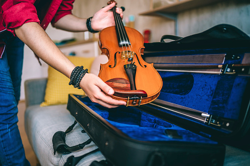 Hands of a man carefully placing his violin in a case