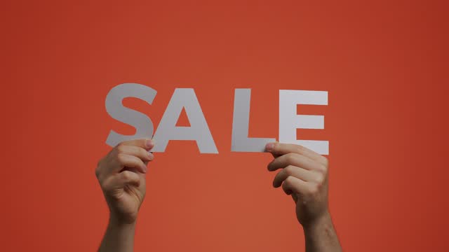 Sale announcement. Hands showing sale sign, close-up video on orange chromakey. Store discounts. Cheap shopping concept