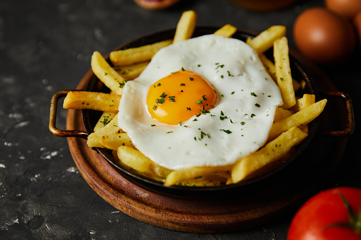 french fries with eggs on top and ingredients on dark background