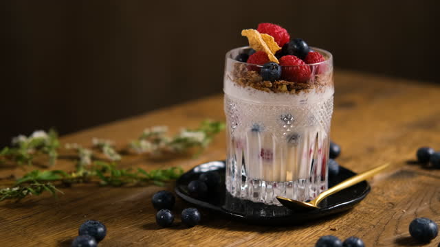 Healthy breakfast - granola, corn flakes and fresh, ripe raspberries and blueberries in a fancy glass standing on a wooden table. Dark style photography. Dark style photography.