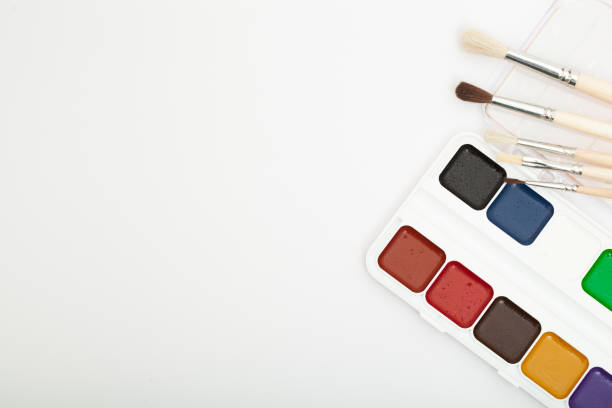 A set of watercolor paints and paint brushes on a white background with a copy space for text. Close-up