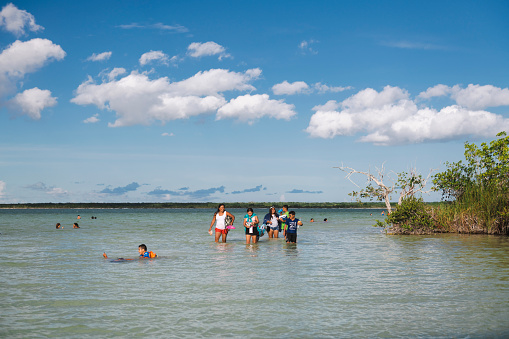Bacalar, Mexico - June 2, 2021: People walk and swim in the shallow waters of  Bacalar Lagoon.