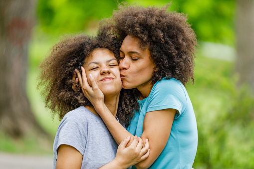 Cute Little Afro Girl with Curly Hair is Happy to Spend a Summer Day With her Lovely Mother Who is Kissing her and Enjoying in Lovely Emotions.
