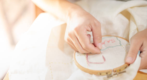 istock Female hand holding wood embroidery frame and needle working on pattern stitching in a process of handiwork. 1325131737