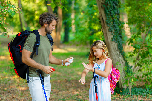 A Young Father and Daughter Hikers with Backpacks have Problems with Itch Because of Large Group of Mosquitoes Attacking Them and They are Using a Preventive Spray.