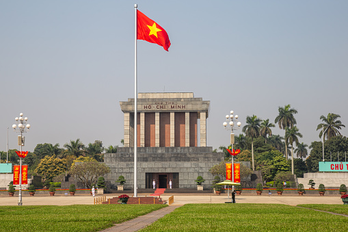 Hanoi, Vietnam – February 21, 2021: Ho Chi Minh Mausoleum in Ba Đình Square.   Hồ Chí Minh was a Vietnamese revolutionary and politician. He served as Prime Minister of North Vietnam from 1945 to 1955 and President from 1945 until his death on 2 September 1969. He was a key figure in the People's Army of Vietnam and the Việt Cộng during the Vietnam War, which lasted from 1955 to 1975. After the defeat of the US-backed Republic of South Vietnam, the country was officially reunified in 1976. Saigon, the former capital of South Vietnam, was renamed Ho Chi Minh City in his honor. His embalmed body is currently on display in the Ho Chi Minh Mausoleum which is guarded 24 hours a day and the national flag flies in Ba Dinh Square