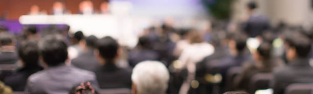 Blurred de-focused audience in conference lecture presentation room. Corporate presentations in conference hall. Seminar speaker giving training to new employees. Presenter in forum workshop event.