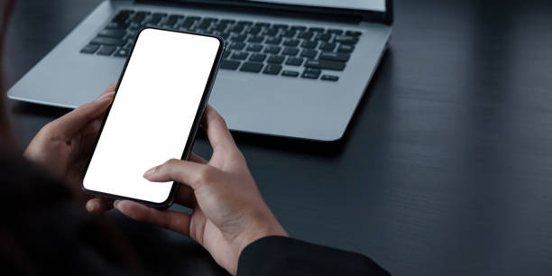 istock Mockup image blank white screen cell phone.women hand holding texting using mobile on desk at home office. 1325146906