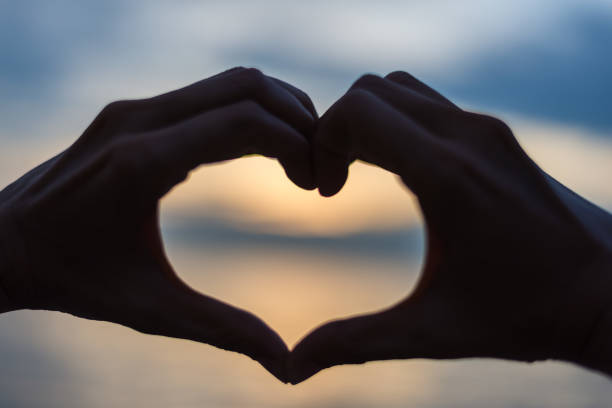 istock Couple doing heart shape with their hands on lake shore 1325148797