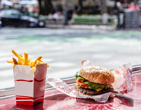 Chessburger and French fries meal on red counter. Blurred background street scene viewed through window.