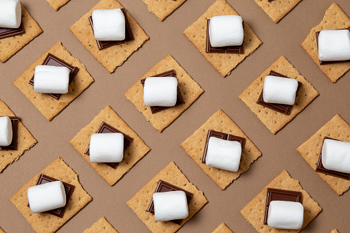 graham cracker squares with chocolate, marshmallows on a brown background. ready to roast. geometric pattern