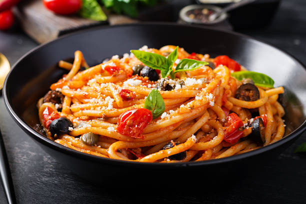 spaghetti alla puttanesca - plato de pasta italiana con tomates, aceitunas negras, alcaparras, anchoas y basi - espagueti fotos fotografías e imágenes de stock