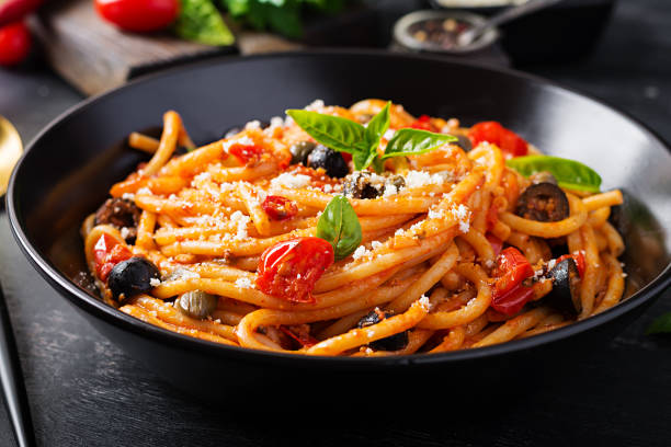 spaghetti alla puttanesca - plat de pâtes italiennes avec tomates, olives noires, câpres, anchois et basi - pâtes fraîches photos et images de collection