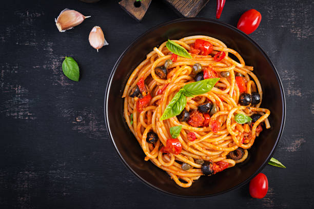 Spaghetti alla puttanesca - italian pasta dish with tomatoes, black olives, capers, anchovies and basil. Top view, flat lay stock photo