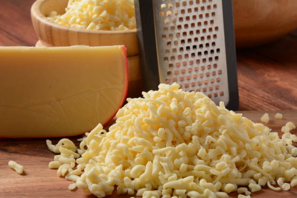 Heap of shredded cheese on small wooden board. Grated cheese for cooking on a cutting board on a wooden background Heap of shredded cheese on small wooden board. Grated cheese for cooking on a cutting board on a wooden background edam stock pictures, royalty-free photos & images
