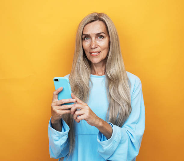 istock Lovely senior lady on yellow background and using modern smartphone 1325185766