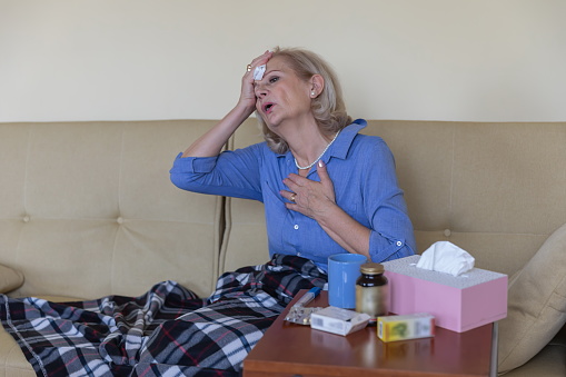 Sick and Depressed Older Woman is Having High Temperature is Using Handkerchiefs in the Bed, Trying to Override the Sickness. Virus COVID-19.