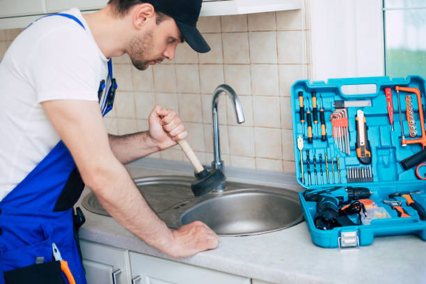 Handyman in uniform is cleaning a clogged kitchen sink with the help of plunger stock photo
