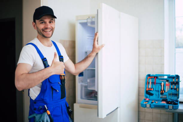 jovem reparador profissional em uniforme de trabalhador e boné com caixa de ferramentas moderna com equipamento após reparo de geladeira na cozinha - coveralls professional occupation manual worker service occupation - fotografias e filmes do acervo