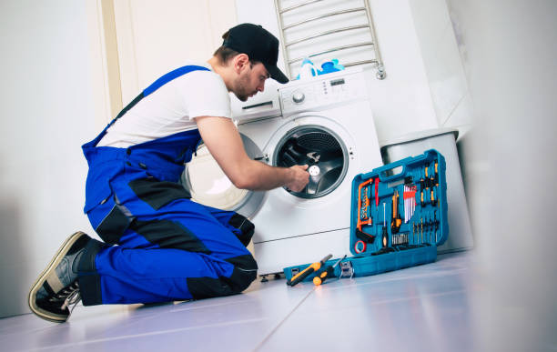 The young handsome repairman in worker suit with the professional tools box is fixing the washing machine in the bathroom stock photo