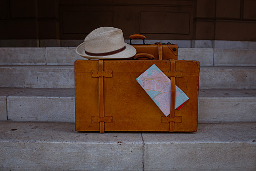 Retro leather coffers, with a sun hat and city map on, left on the steps