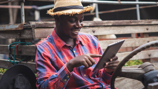 African farmer using tablet and smiling while sitting in the tractor.Agriculture or cultivation concept.16:9 style stock photo