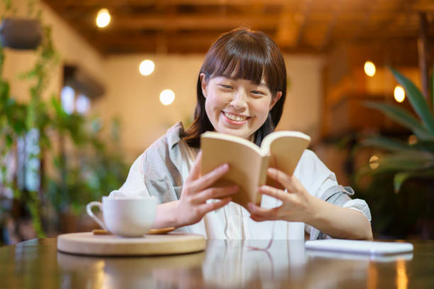 une jeune femme lisant un livre - le monde des cafés photos et images de collection