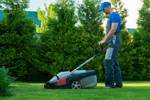 Young gardener in overalls uses a lawn mower on the plot.