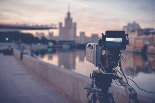 eine professionelle videokamera steht auf einem stativ, das die stadt und den fluss bei sonnenaufgang aufzeichnet, dokumentarfilme in moskau - television camera tripod media equipment videography stock-fotos und bilder