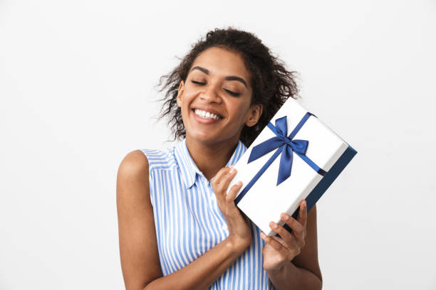 Happy young african woman posing isolated over white wall background holding present gift box. Image of a beautiful happy young african woman posing isolated over white wall background holding present gift box. alternative pose stock pictures, royalty-free photos & images