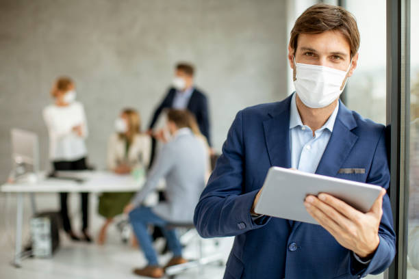istock Handsome young business man wearing protective facial mask while holdind digital tablet 1325207628