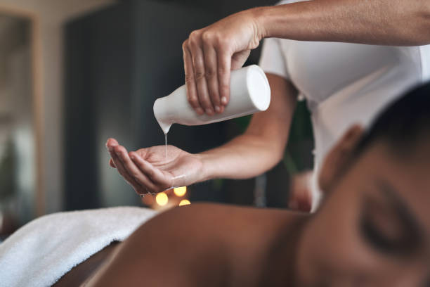 primer plano de un masajista vertiendo aceite corporal en sus manos mientras da un masaje a un cliente en un spa - massage therapist fotografías e imágenes de stock