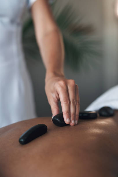 gros plans d’une femme méconnaissable recevant un massage aux pierres chaudes dans un spa - massaging spa treatment stone massage therapist photos et images de collection