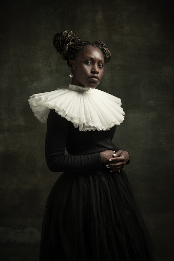 Noblewoman with white pearl. Medieval African young woman in black vintage dress with big white collar isolated on dark green background. Concept of comparison of eras, modernity and renaissance.