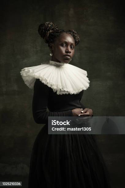 Portrait Of Medieval African Young Woman In Black Vintage Dress With Big White Collar Posing Isolated On Dark Green Background Stock Photo - Download Image Now