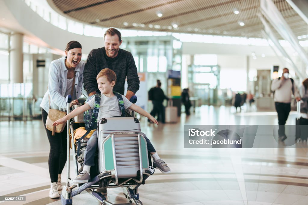 Couple pushing trolley with their child at airport Couple happily pushing the trolley with their son at airport. Child enjoying sitting on luggage trolley while parents pushing it at airport. Travel Stock Photo