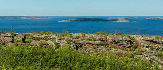 Panorama of seascape with rocks and boulders in foreground. White Sea, Russia, view of archipelago of Kuzova from a high point. Islands, sea, sky and rocky coast in northern latitudes on sunny day.