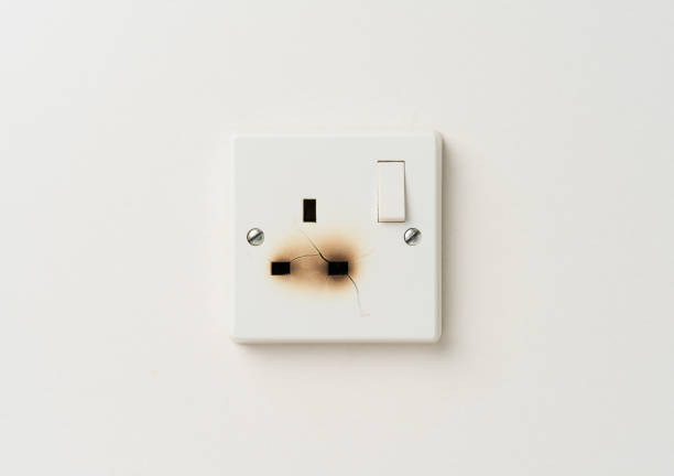 Broken electrical domestic power socket with cracks and burn marks on a white wall stock photo