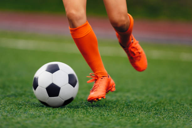 il calciatore colpisce la palla sul tappeto erboso artificiale. calciatore con tacchette sportive che calciano palla. gambe di calciatore che giocano la partita di competizione - soccer socks foto e immagini stock